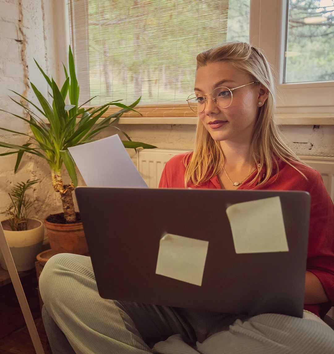 Eine junge Frau sitzt auf dem Sofa am Laptop.