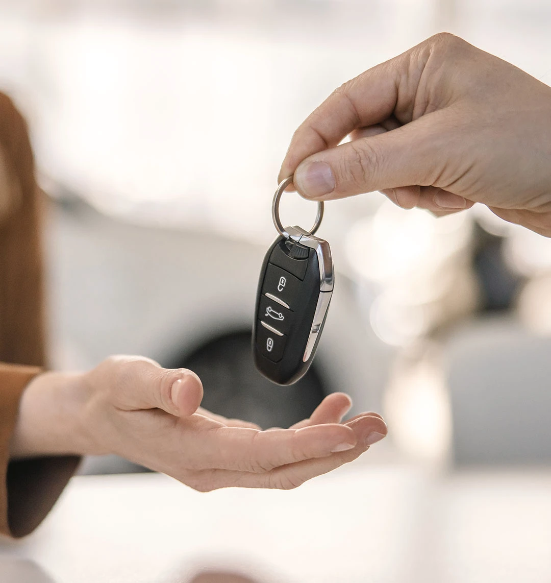 Eine Person reicht einer anderen Person einen Autoschlüssel. Im Fokus stehen dabei die Hände und der Schlüssel.