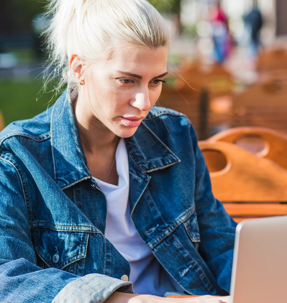 Im Bild ist eine Frau zu sehen, die fokussiert auf ihren Laptop blickt. Die Sonne scheint von der Seite auf ihr Gesicht.