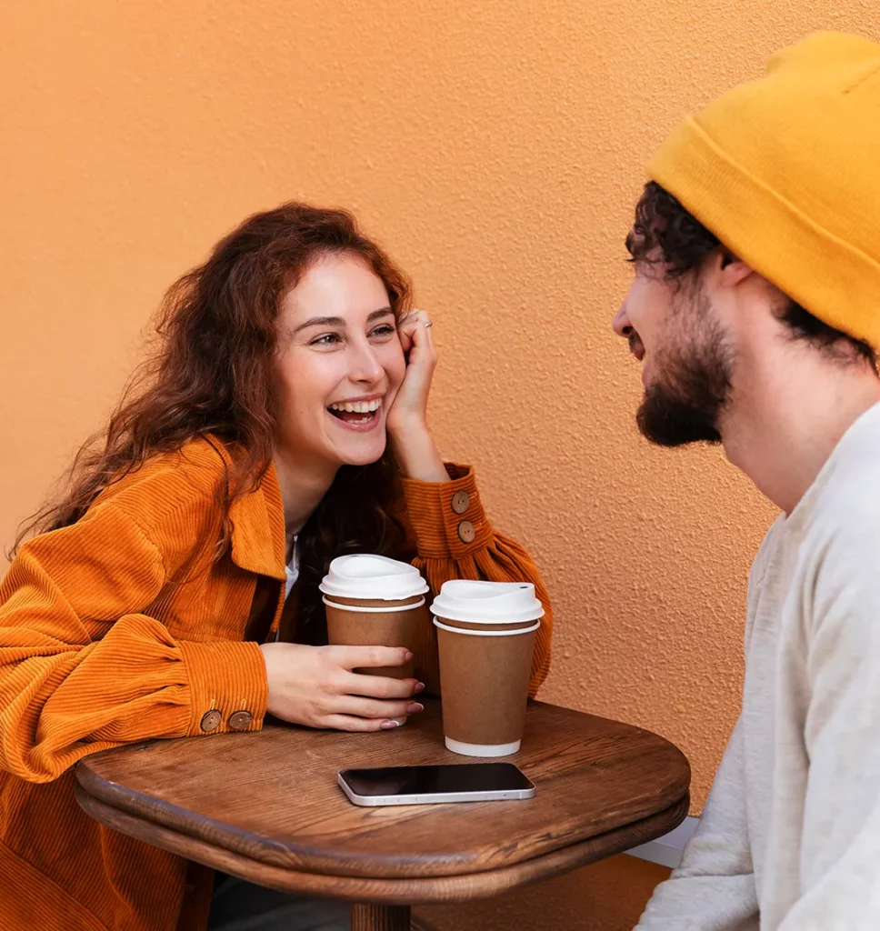 Ein Paar sitzt an einem Tisch. Sie trinken Kaffee und lachen sich an.